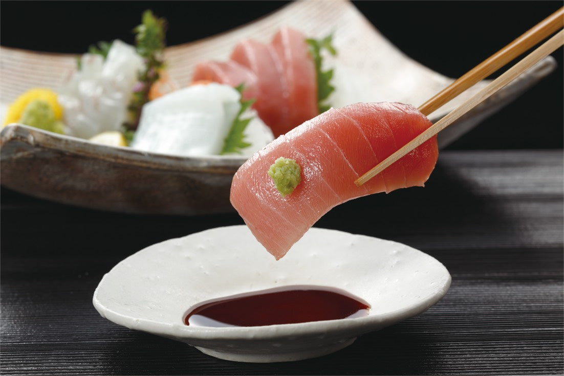 Man dipping sashimi into soy sauce with chopsticks