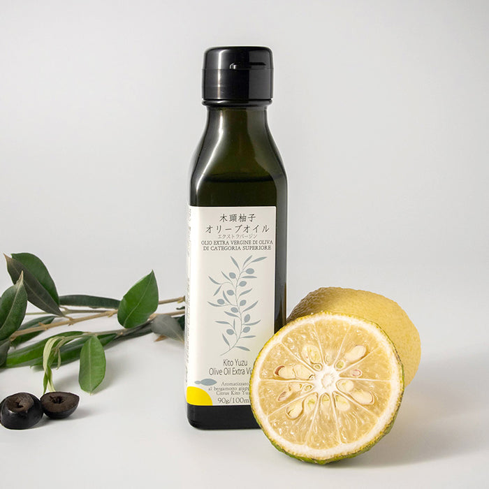 A package bottle of the product next to a half cut yuzu and olive