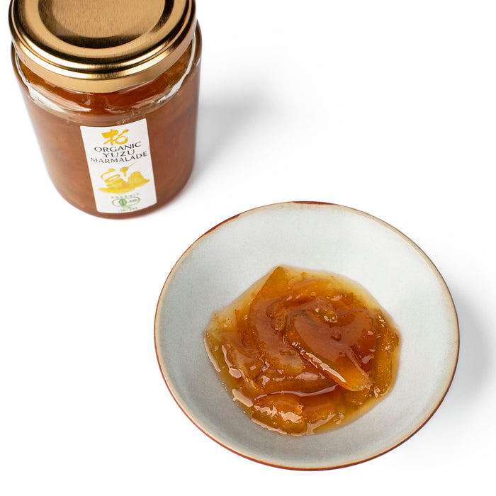 A small ceramic bowl of organic yuzu marmalade next to bottle of the product
