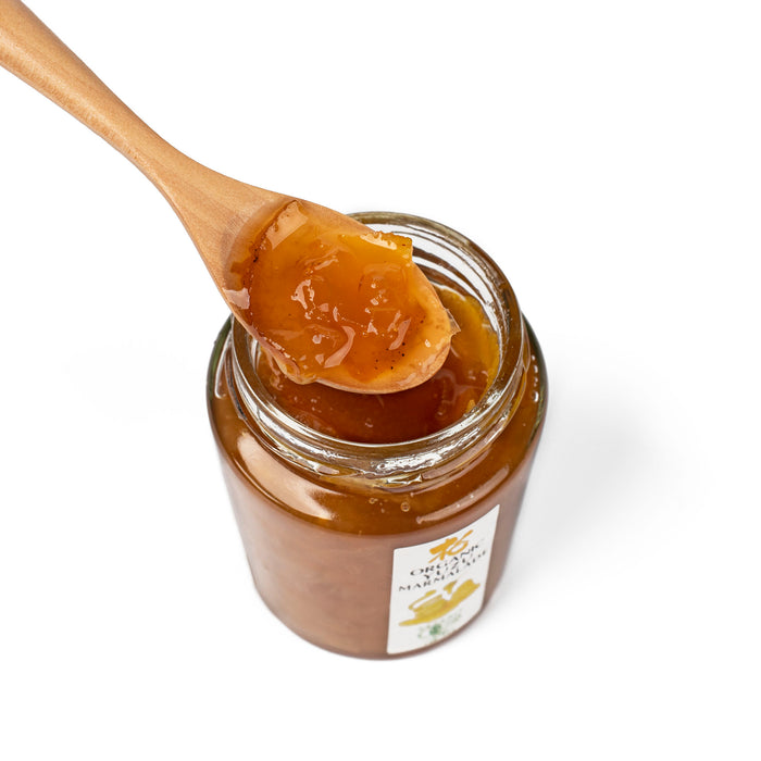 A wooden spoon of organic yuzu marmalade over opened bottle of the product