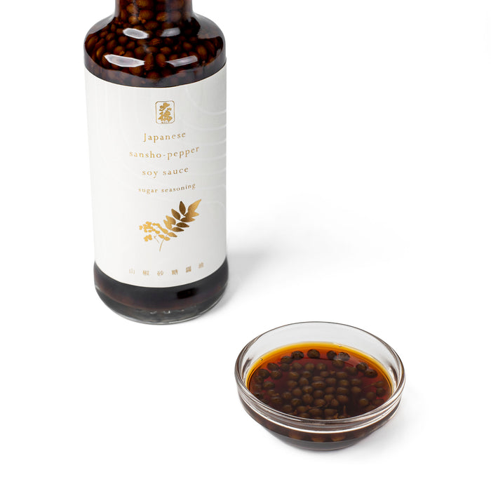 A small glass bowl of sansho pepper soy sauce next to bottle of the product