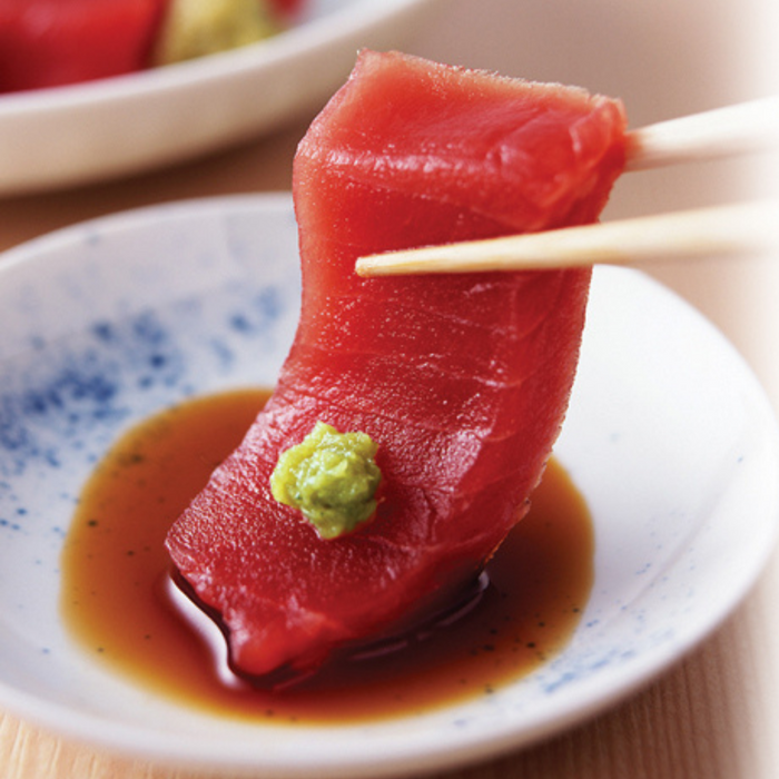 A piece of tuna sashimi topped with coarsely grated hon wasabi being picked up by chopsticks