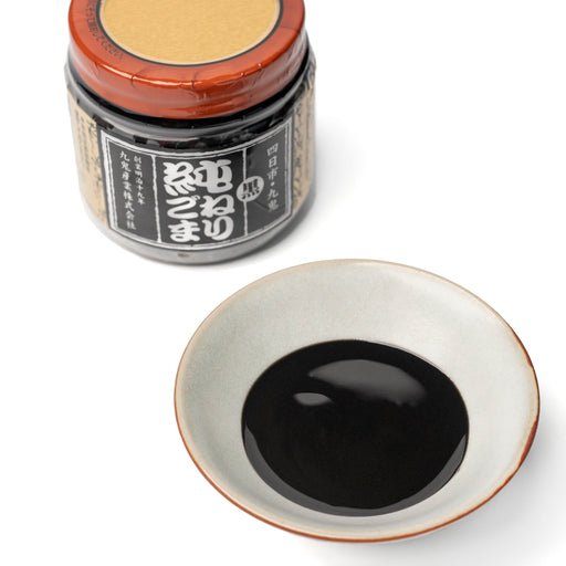 A small bowl of black sesame paste next tp bottle of the product