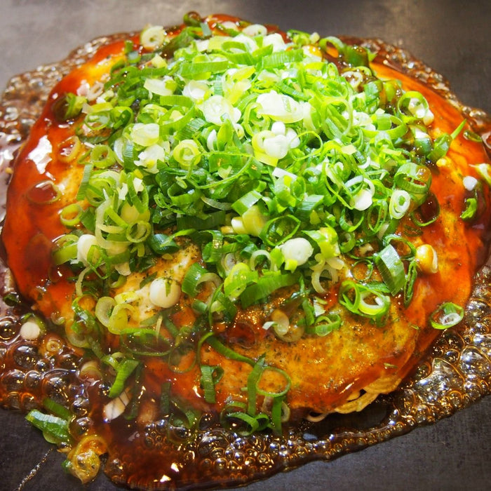 An okonomiyaki pancake topped with scallion and okonomiyaki sauce