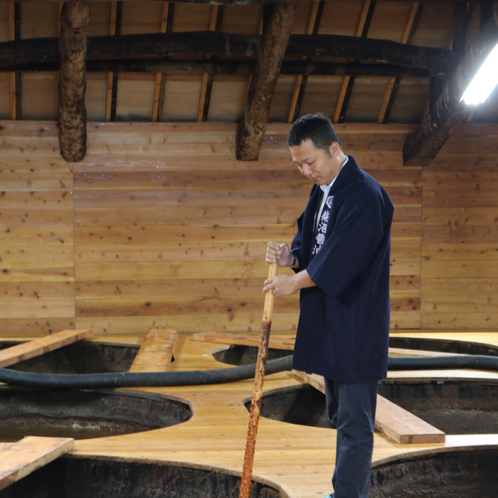 Man stirring soy sauce with wooden stick