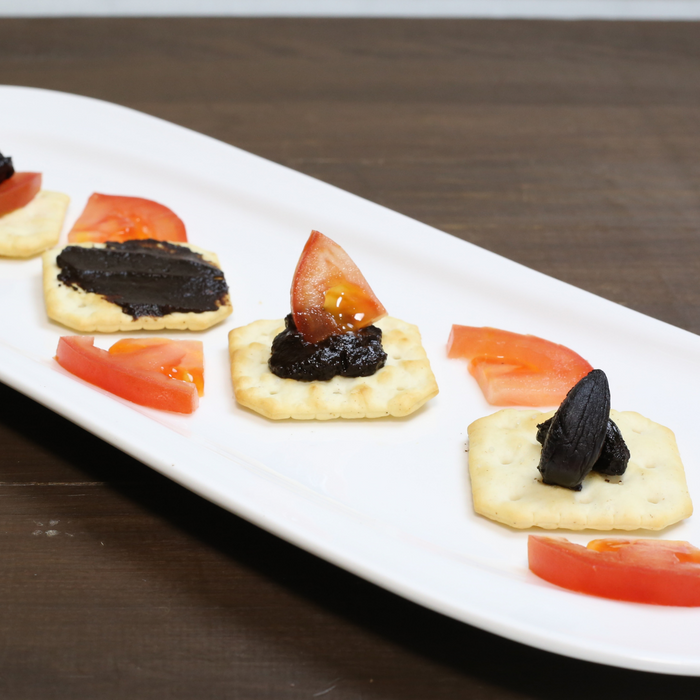 A plate of crackers topped with black garlic