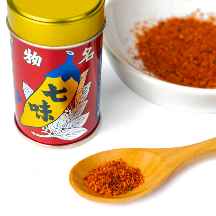 A spoon of shichimi togarashi pepper powder next to a bottle of the product and a bowl of shichimi togarashi pepper powder