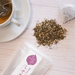 Shiso tea leaves and package bag of the product next to a cup of tea with tea bag