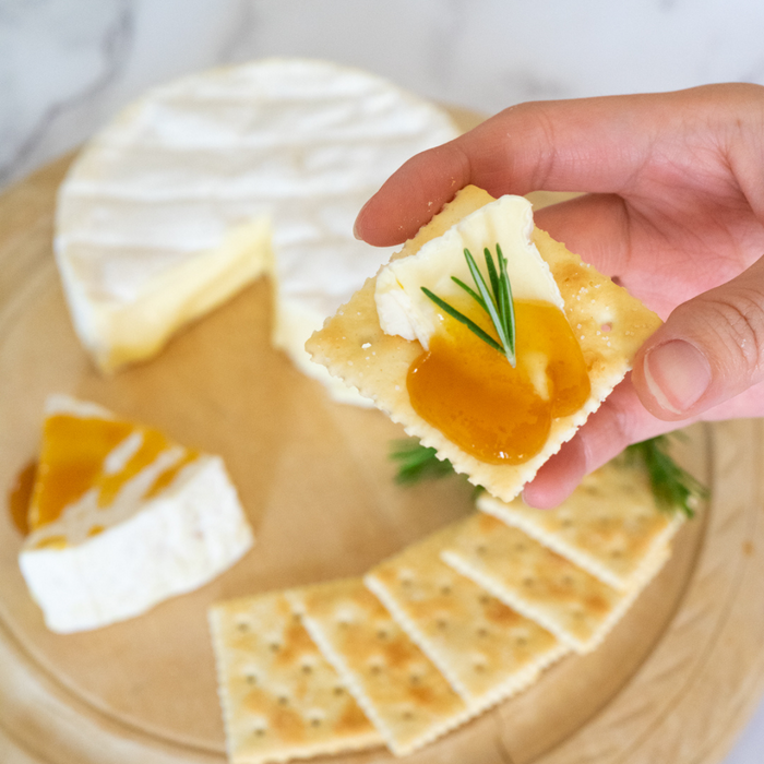 Man taking a piece of cracker topped with cheese and organic yuzu spread by hand