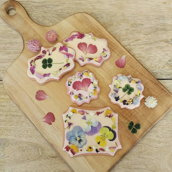 Five kinds of icing cookies topped with a variety of dried edible flowers on wooden cutting board