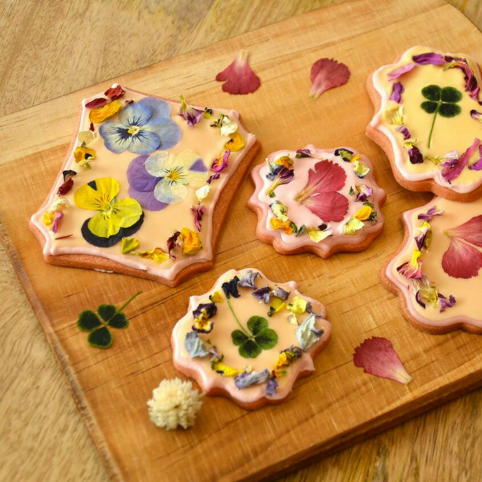 Five pieces of icing cookies topped with dried edible flowers on wooden board