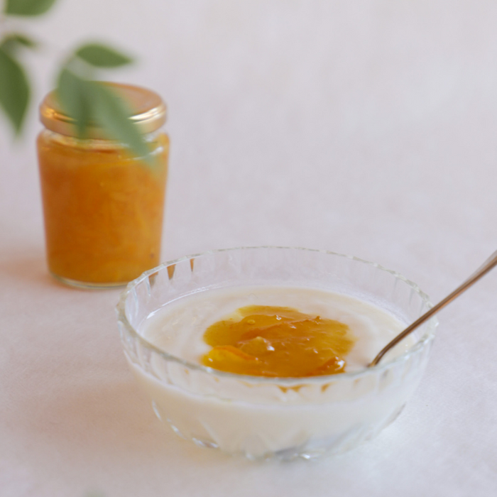 A bowl of yogurt topped with organic yuzu marmalade next to bottle of the product