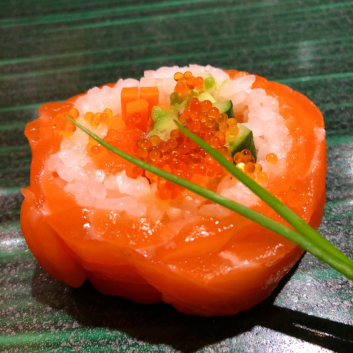 A salmon wrapped sushi roll topped with salmon roe