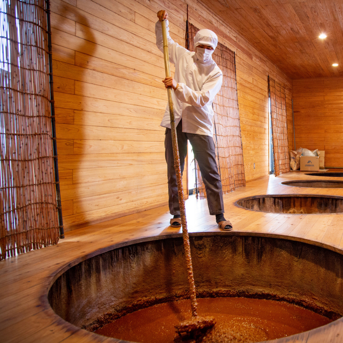 A man stirring soy sauce with a large stick