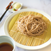 A plate of cold juwari soba noodles next to garnish and a cup of dipping sauce