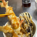 Man taking a deep fried shrimp from tempura rice bowl with chopsticks
