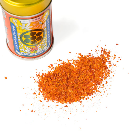 Scattered ichimi pepper next to bottle of the product