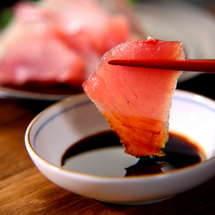 Man taking a slice of sashimi soaked with the organic smoked soy sauce by chopsticks