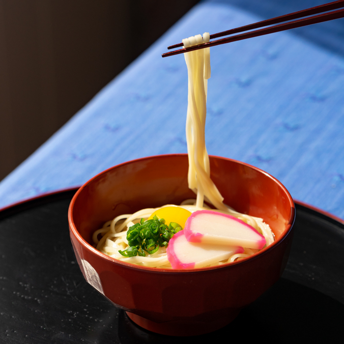 Man taking udon noodles from bowl with chopsticks