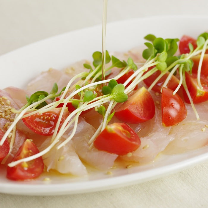 A plate of white fish carpaccio being drizzled with sesame oil