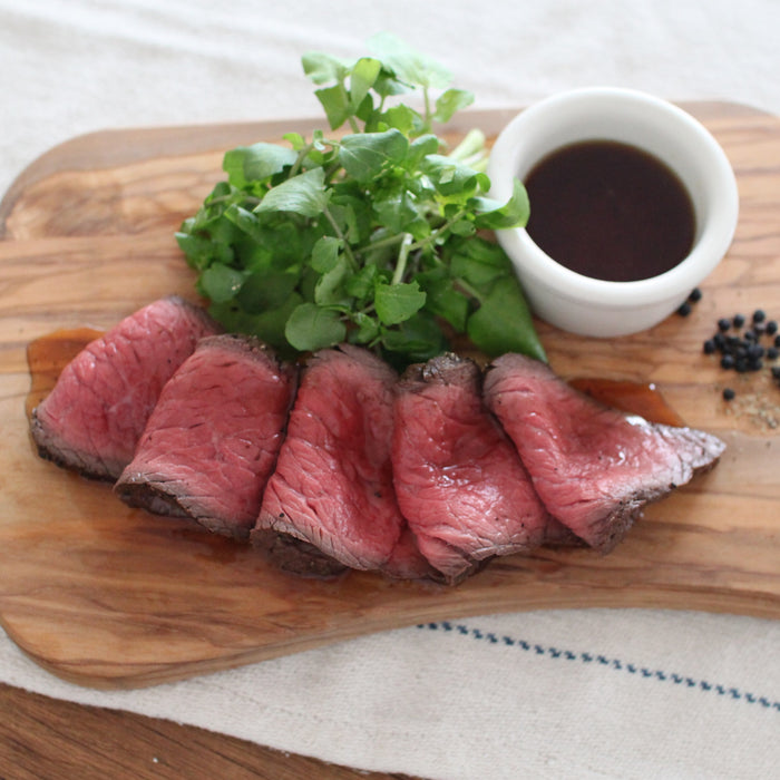 Five slices of roast beef topped with truffle infused soy sauce on wooden board
